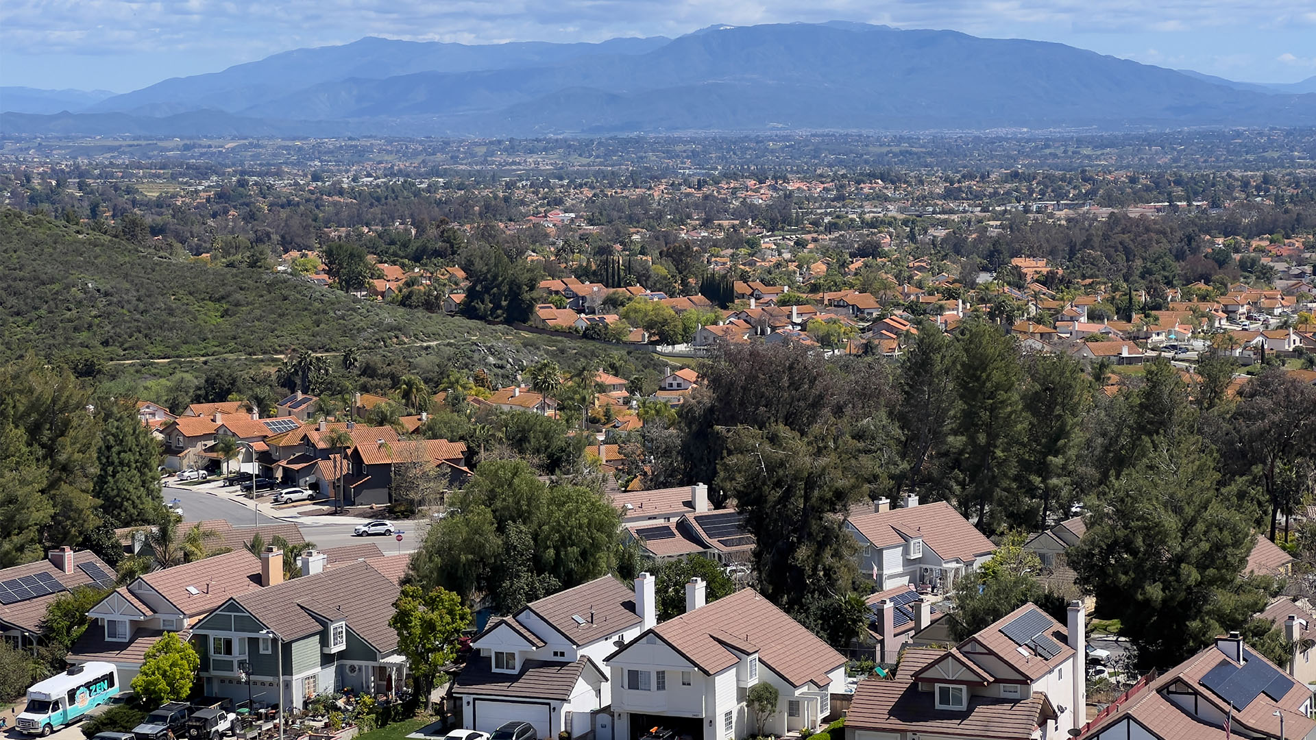 View from a hillside neighborhood in Murrieta, CA toward Palomar Mountain, with suburban homes in the foreground and broad blue mountain ridges beneath scattered clouds.